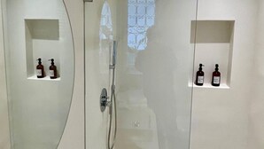A bathroom with two sinks, each with a bottle of soap. There is a shower area with a glass door and a window with a decorative pattern.