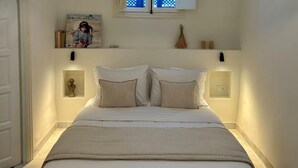 A neatly made bed with two pillows, a small shelf above with a painting and a decorative item, and two wall-mounted lights.