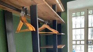 A room with wooden hangers on a wall-mounted rack, a window with decorative iron bars, and a green wall.