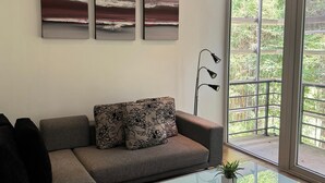 Una sala de estar moderna con un sofá gris, una mesa de centro de vidrio y tres cuadros abstractos en la pared.