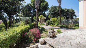 Un jardín con un camino de piedra, diversas plantas y una pequeña construcción.