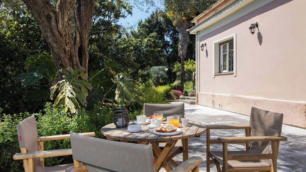Una mesa redonda de madera con sillas, una disposición para el desayuno y un edificio con ventana y lámpara en la pared.