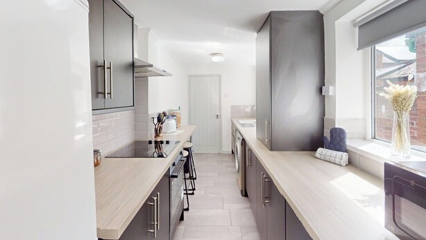 A modern kitchen with a central island, built-in appliances, and a large window providing natural light. - Cosy Home in Sunderland (Sunderland)