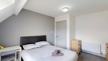 A bedroom with a bed, a desk, a radiator, and a door.