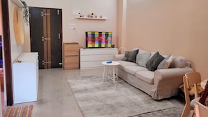 A living room with a sofa, a small table, a TV, and a refrigerator. - Charming 1-bedroom apartment with WiFi, AC in vibrant Goa (Goa)