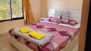 A neatly made bed with pink and white bedding, a window with curtains, and a wall with framed pictures. - Charming 1-bedroom apartment with WiFi, AC in vibrant Goa (Goa)