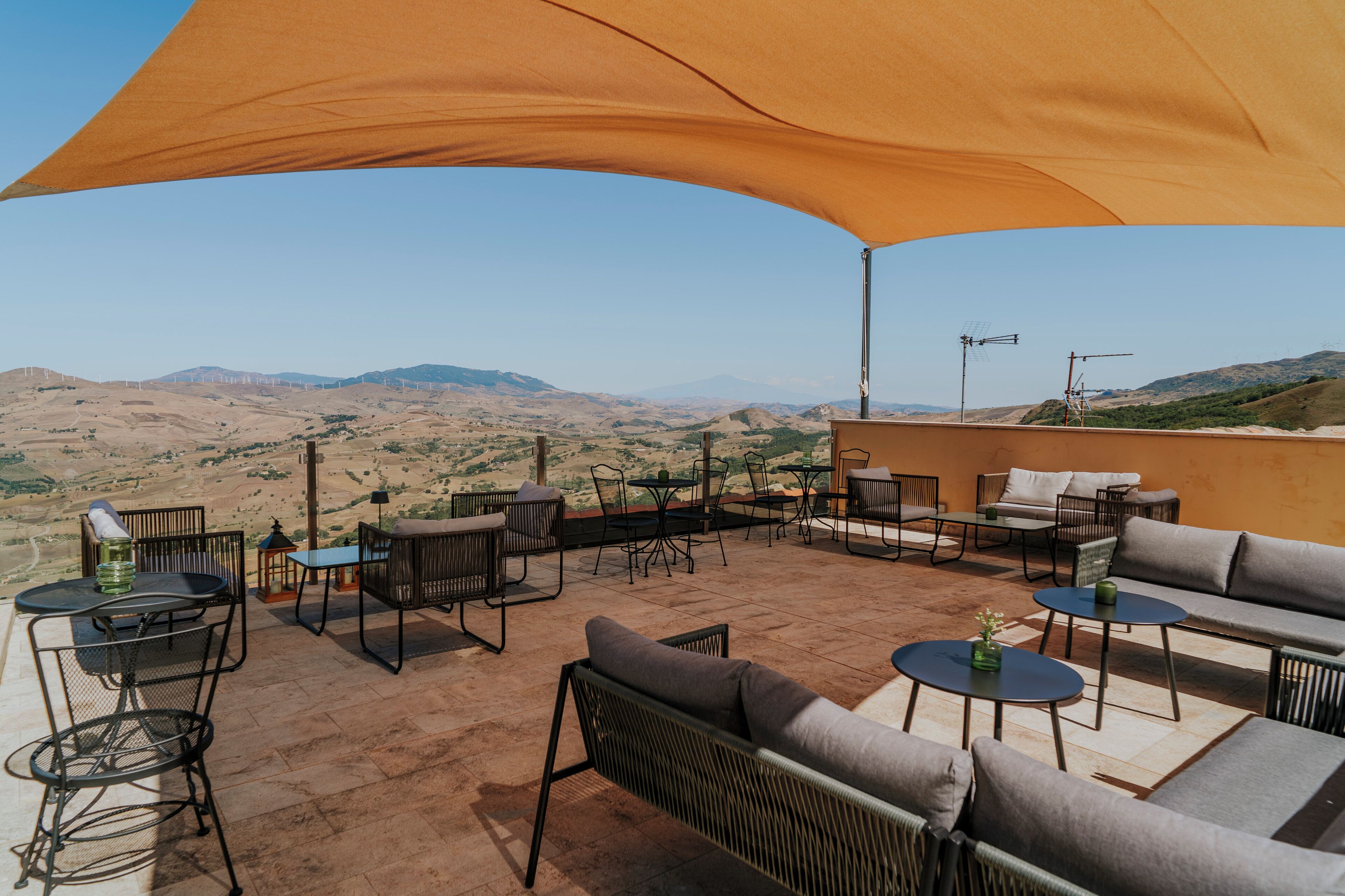 Un patio exterior con mesas y sillas, con vistas a un paisaje montañoso.