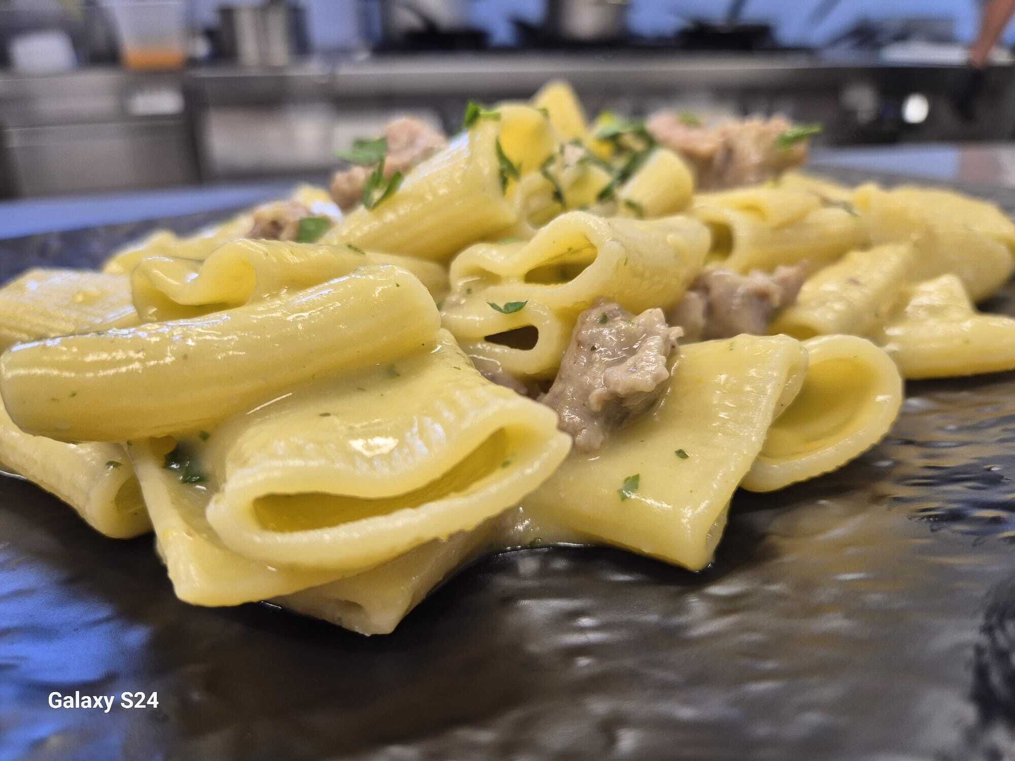 A plate of pasta with a creamy sauce and meat, served on a dark plate.