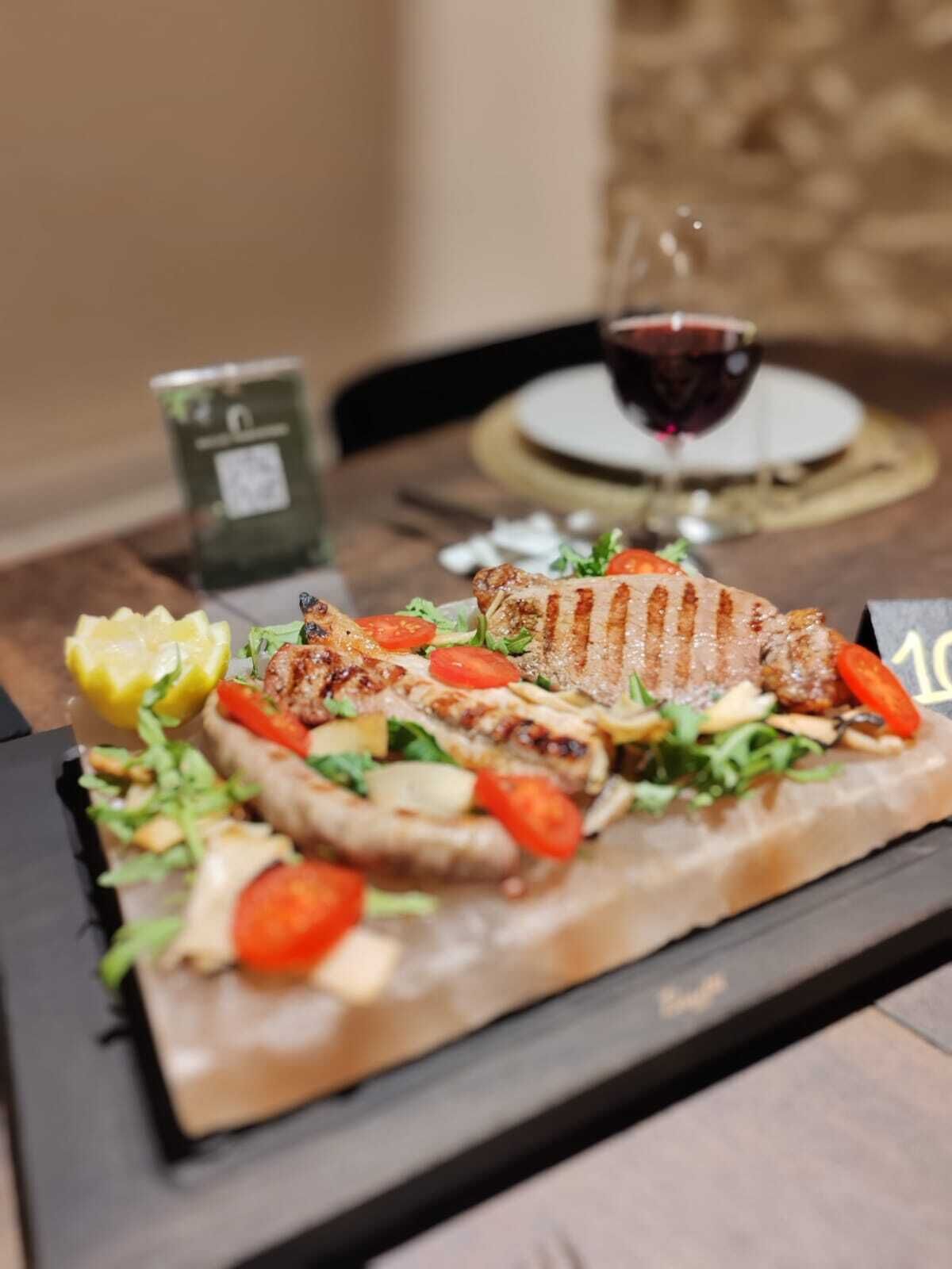 A plate of grilled meat with vegetables and a lemon wedge on a black slate plate.
