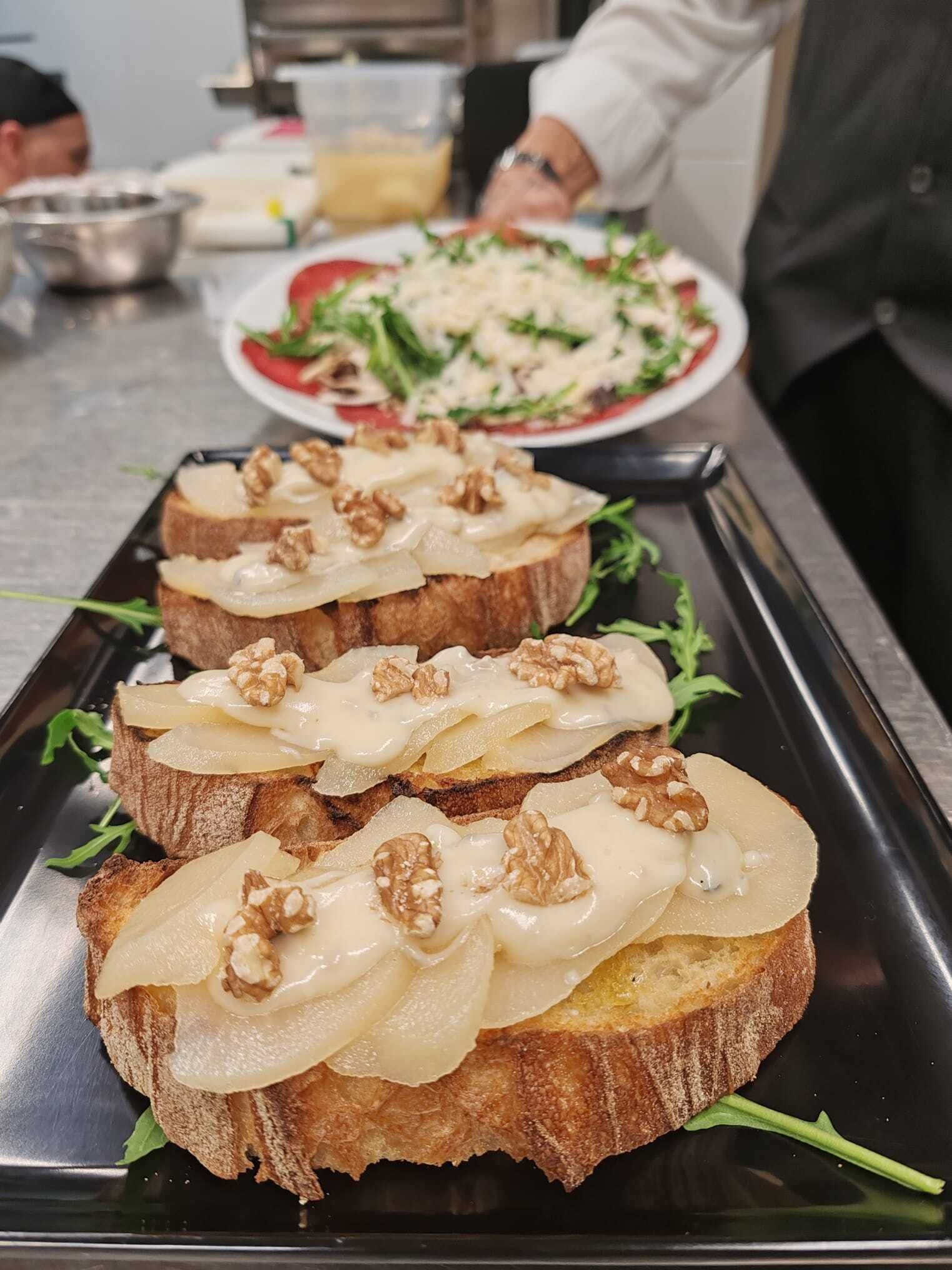 Un plato con pan cubierto de queso y nueces, adornado con hojas verdes, en una cocina.