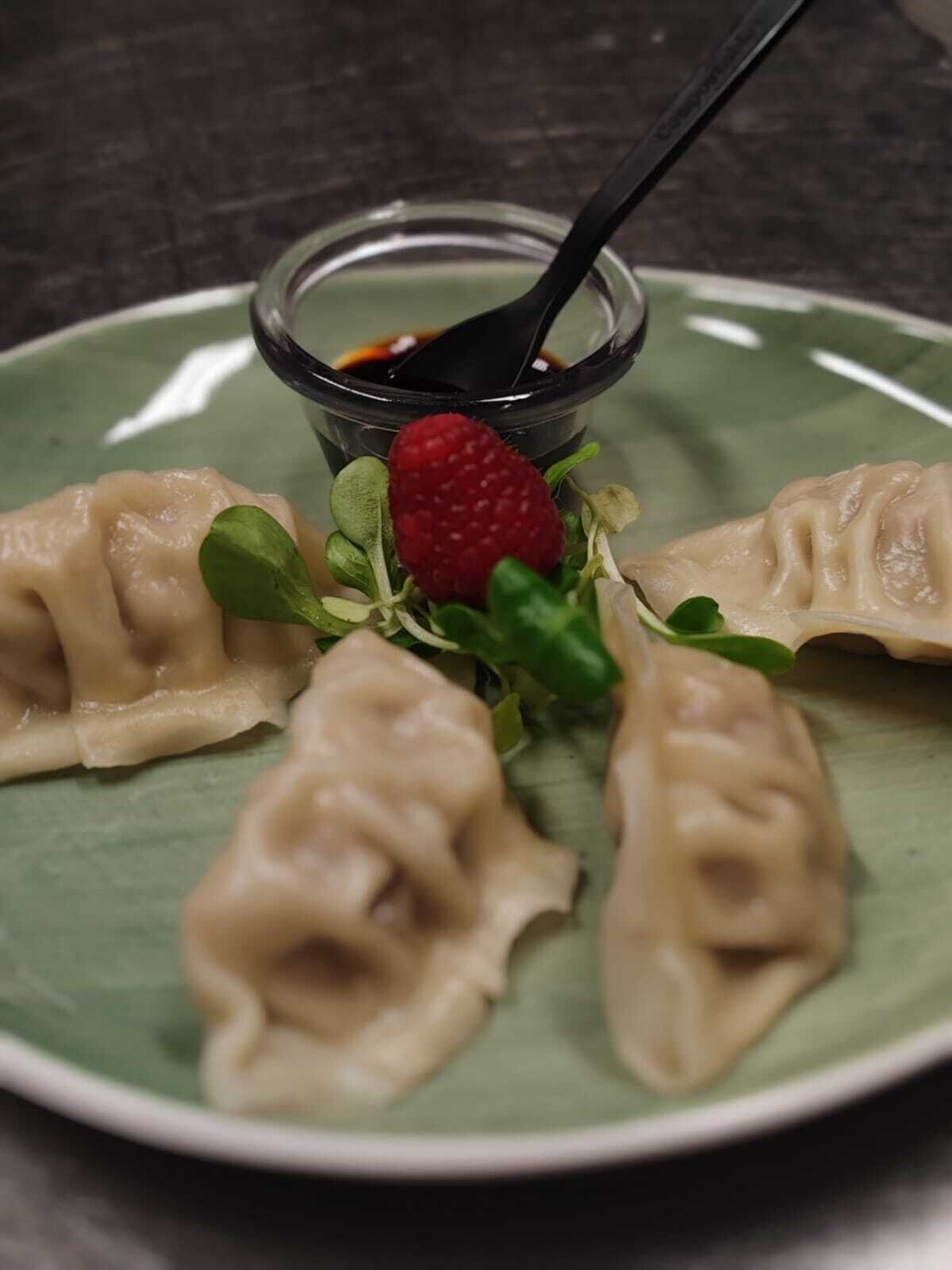 Un plato de dumplings, un tazón pequeño de salsa y una fresa.