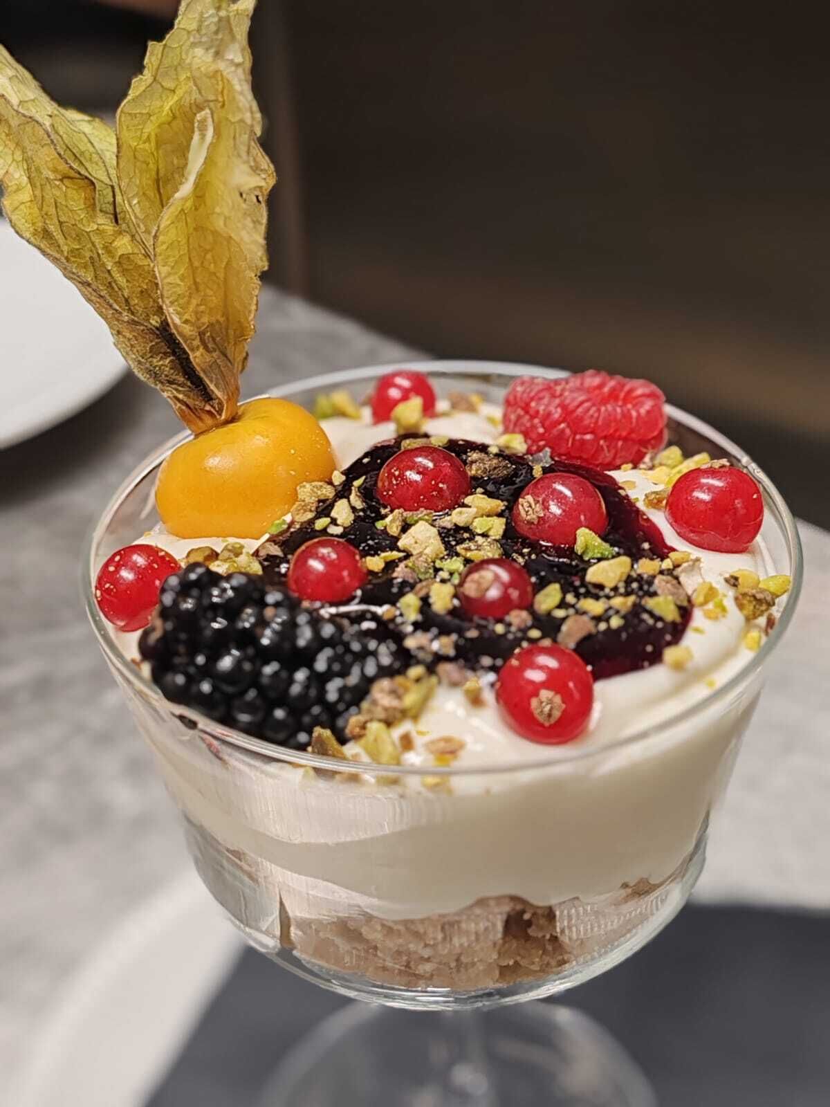 A dessert in a clear glass bowl with various fruits and nuts on top.