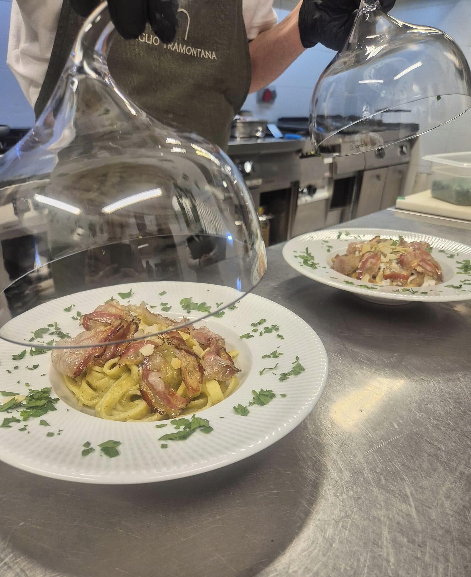 Una encimera de cocina con dos platos de pasta, bacon y hierbas para decorar.