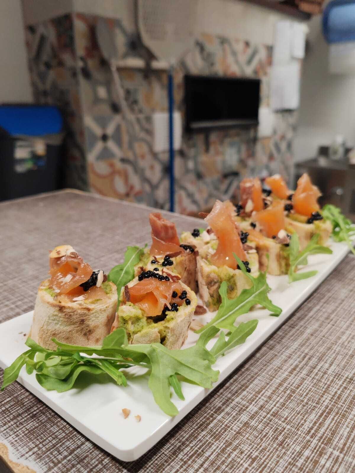 A long white rectangular plate with food items arranged in a row, garnished with green leaves.