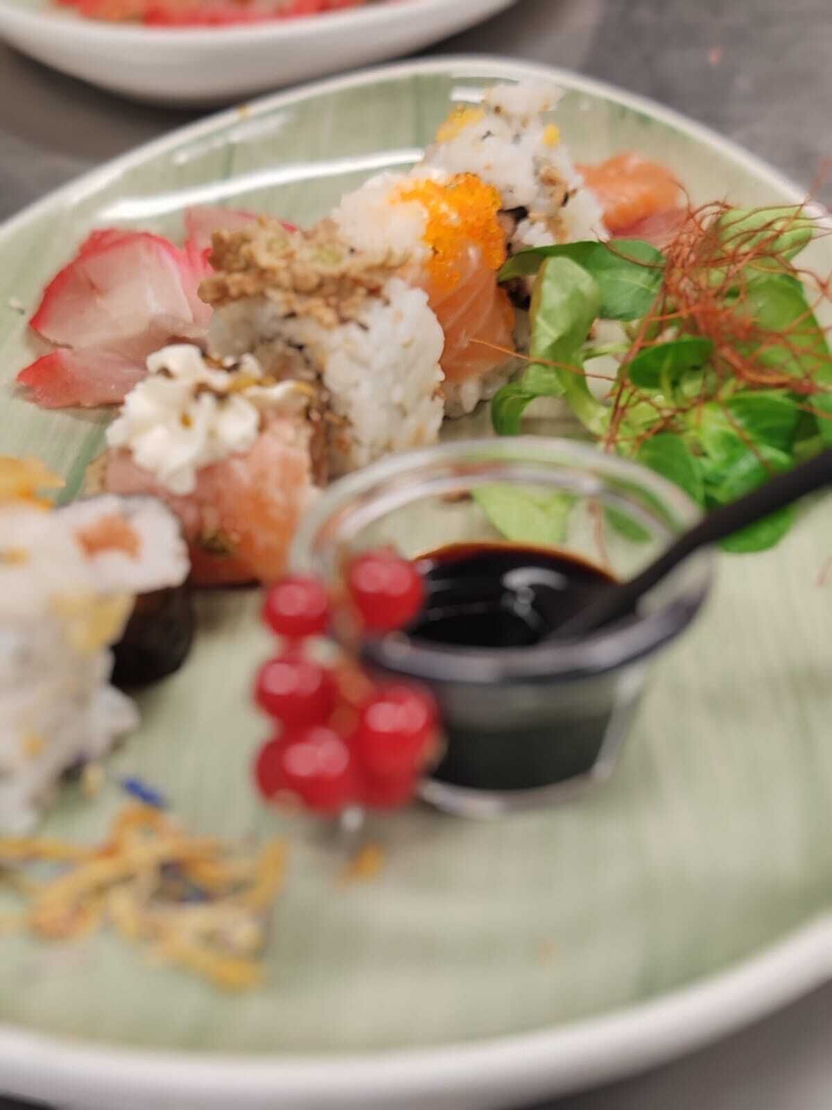 A plate of sushi with various toppings and a small bowl of soy sauce.
