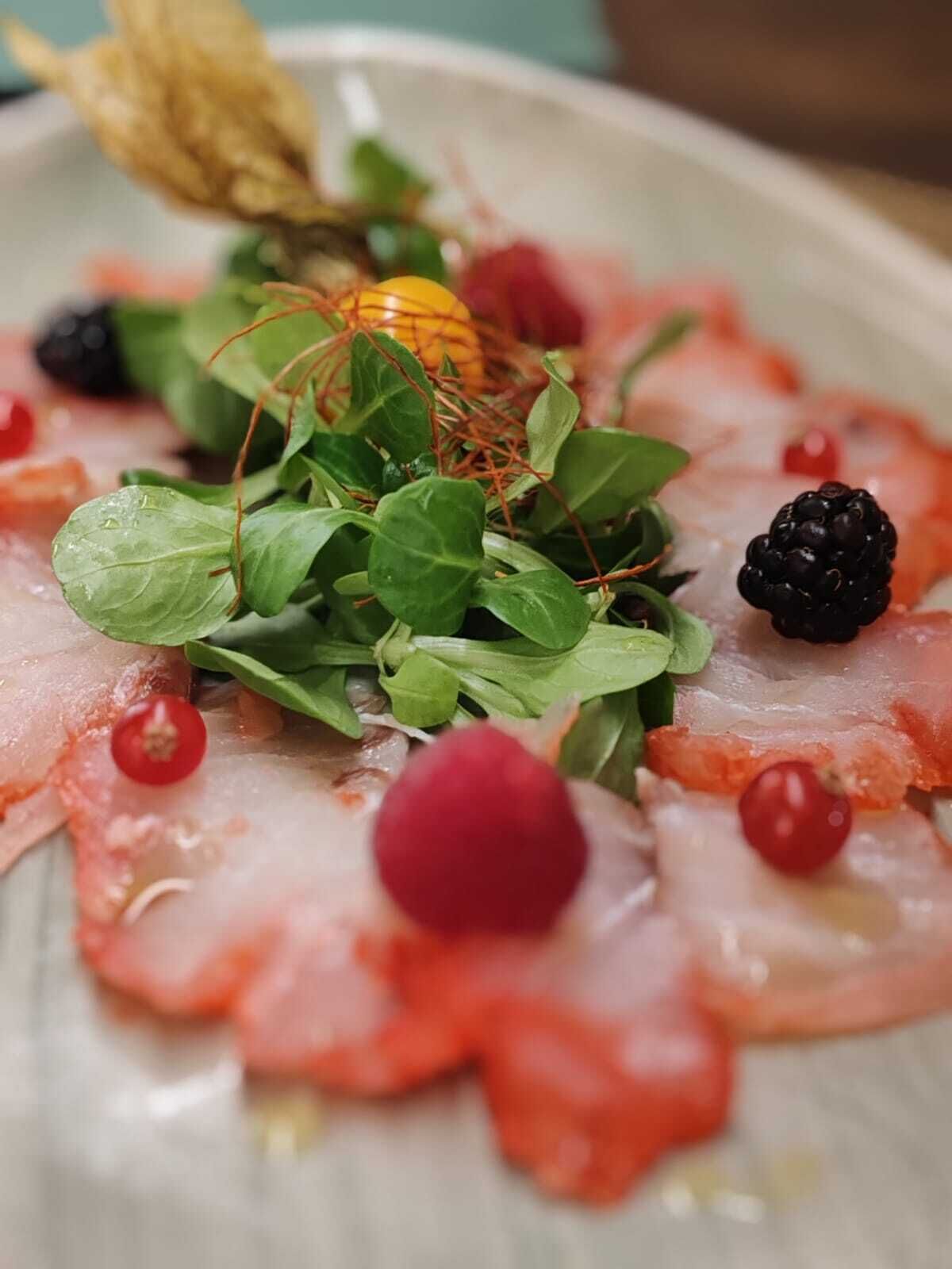 A plate with thinly sliced meat, fresh greens, and berries.