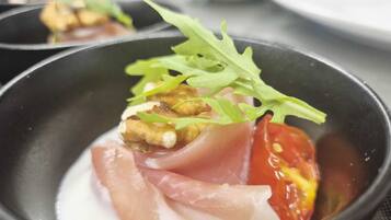 A dish with prosciutto, tomato, and greens in a black bowl.