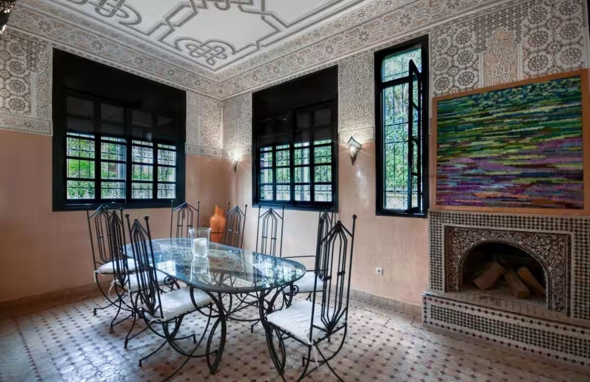 A dining area with a glass table and chairs, large windows, and a patterned floor.