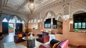 Um interior luxuoso com arcos ornamentados, uma área de estar central com sofás de couro e um teto decorativo.