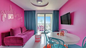 A modern room with a pink sofa, a white table with chairs, and a TV mounted on the wall. - Żurawie Pink Port by Grand Apartments (Gdańsk)