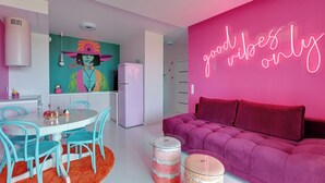 A modern kitchen with a white refrigerator, a dining table with turquoise chairs, and a vibrant pink wall with a neon sign. - Żurawie Pink Port by Grand Apartments (Gdańsk)