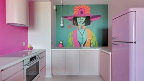 A modern kitchen with a pink refrigerator, white cabinets, and a colorful mural on the wall. - Żurawie Pink Port by Grand Apartments (Gdańsk)