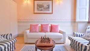A living room with a white sofa, pink cushions, a chessboard, striped armchairs, and a framed painting on the wall. - Venus apartment (Firenze)