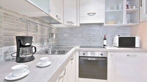 A modern kitchen with a coffee maker, microwave, oven, and white cabinetry. - Venus apartment (Firenze)
