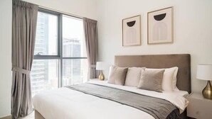 A modern hotel room with a large bed, a nightstand, two framed pictures, and a window with curtains.