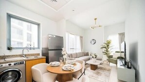 A compact apartment with a kitchen, dining area, and living room. It includes a washing machine, a dining table with chairs, a sofa, a TV, and a small side table.