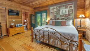 Un dormitorio de cabaña de madera con cama, cómoda, televisor y un tapiz acolchado.