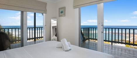 A hotel room with a large bed, a bathroom with a mirror, and a balcony with a view of the ocean.