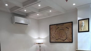 A room with two yellow tufted sofas, a white coffee table, an air conditioning unit, a framed map, and a sculpture on the wall. - GREEN GARDEN CAFE & HOTEL (Amritsar)