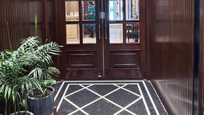 A hotel lobby with a geometric patterned floor, wooden paneling, and a large double door with glass panels. - GREEN GARDEN CAFE & HOTEL (Amritsar)