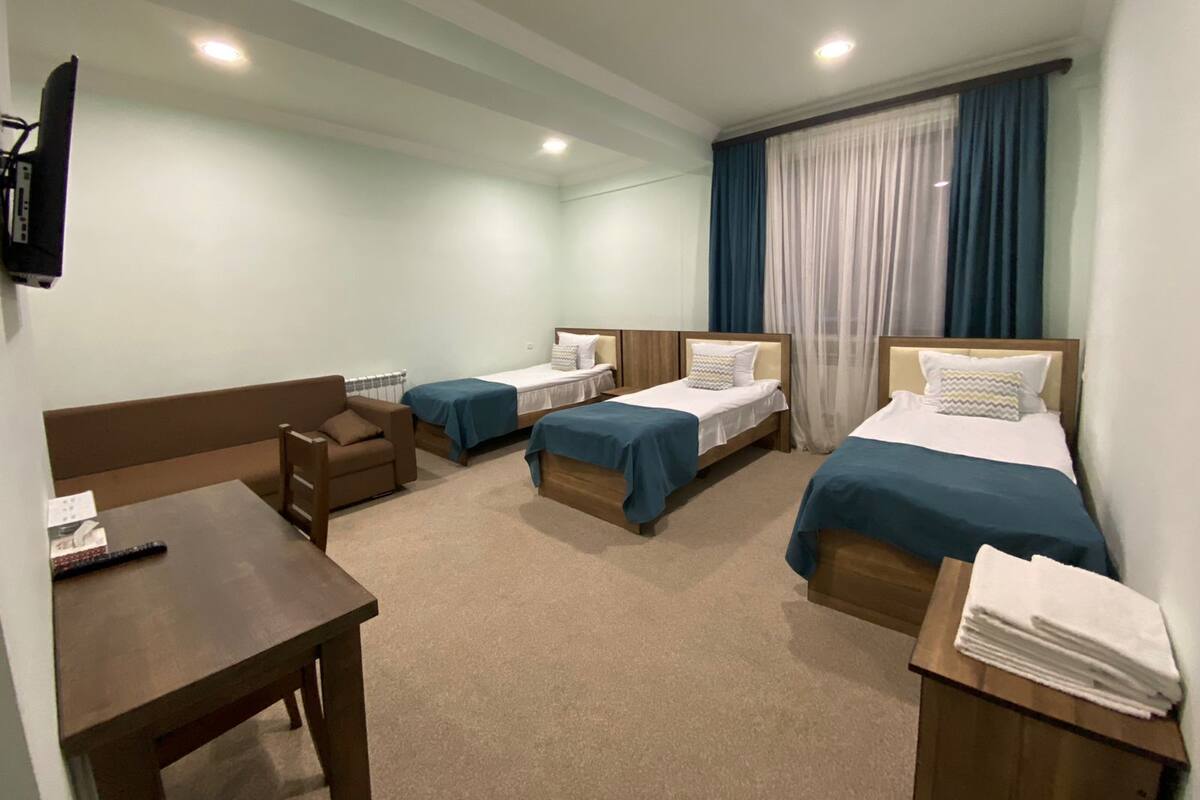 Habitación de hotel con tres camas, un escritorio, una silla y un televisor.
