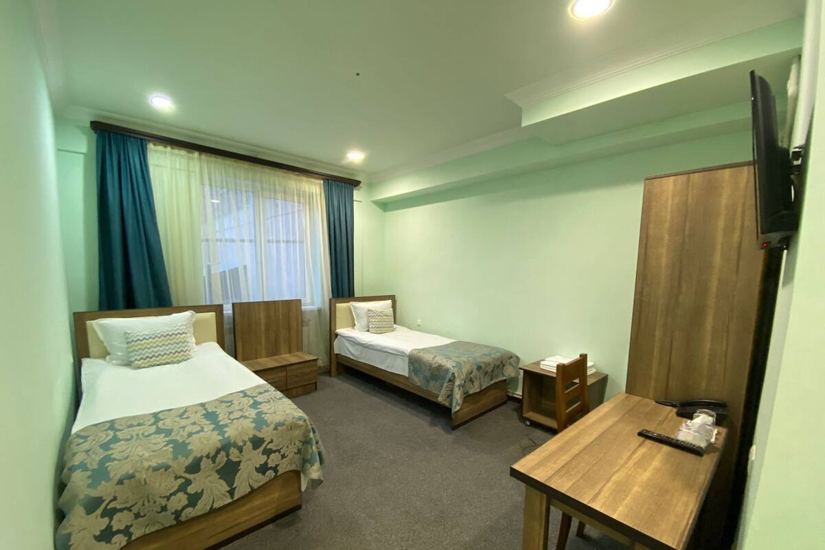 Una habitación de hotel con dos camas individuales, un escritorio de madera, un televisor y una ventana con cortinas.
