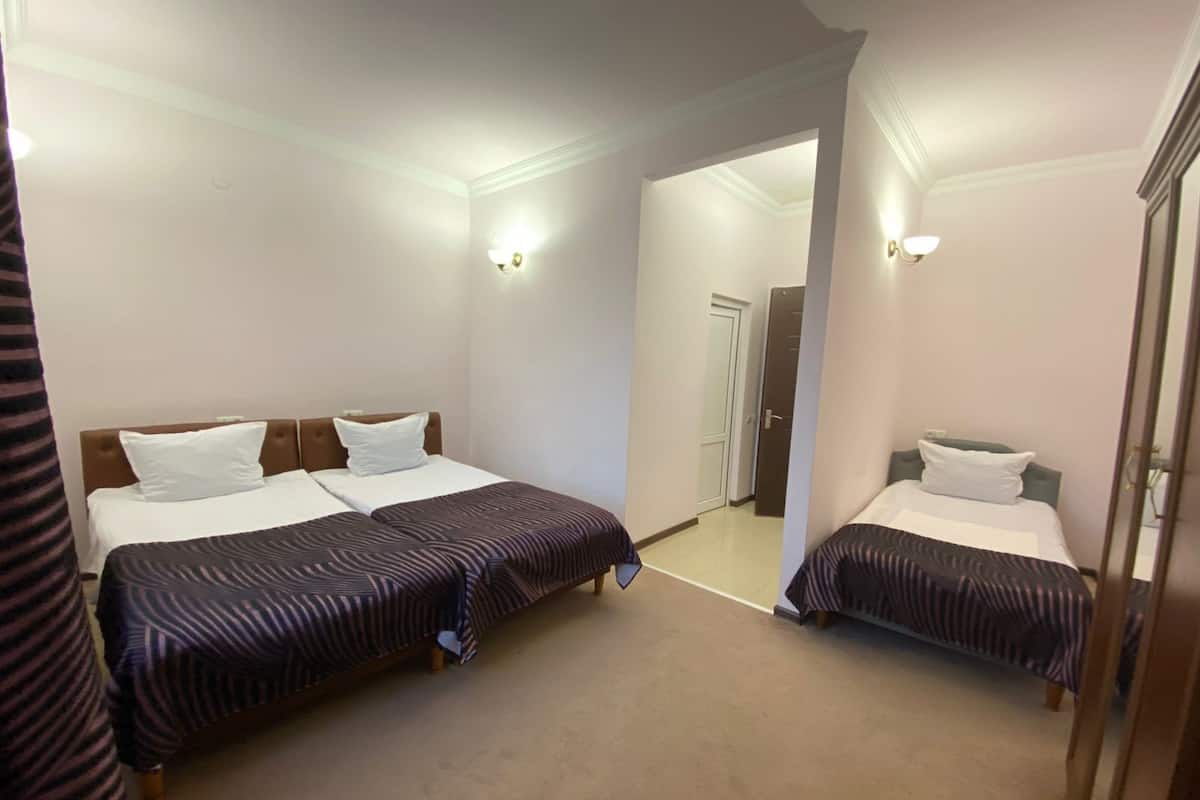 Habitación de hotel con dos camas, cada una con cabecera y almohada. Hay luces fijadas a la pared y una puerta que da a otra habitación.