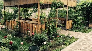 Una estructura de madera rústica con techo de paja, rodeada por un jardín con diversas plantas y flores.