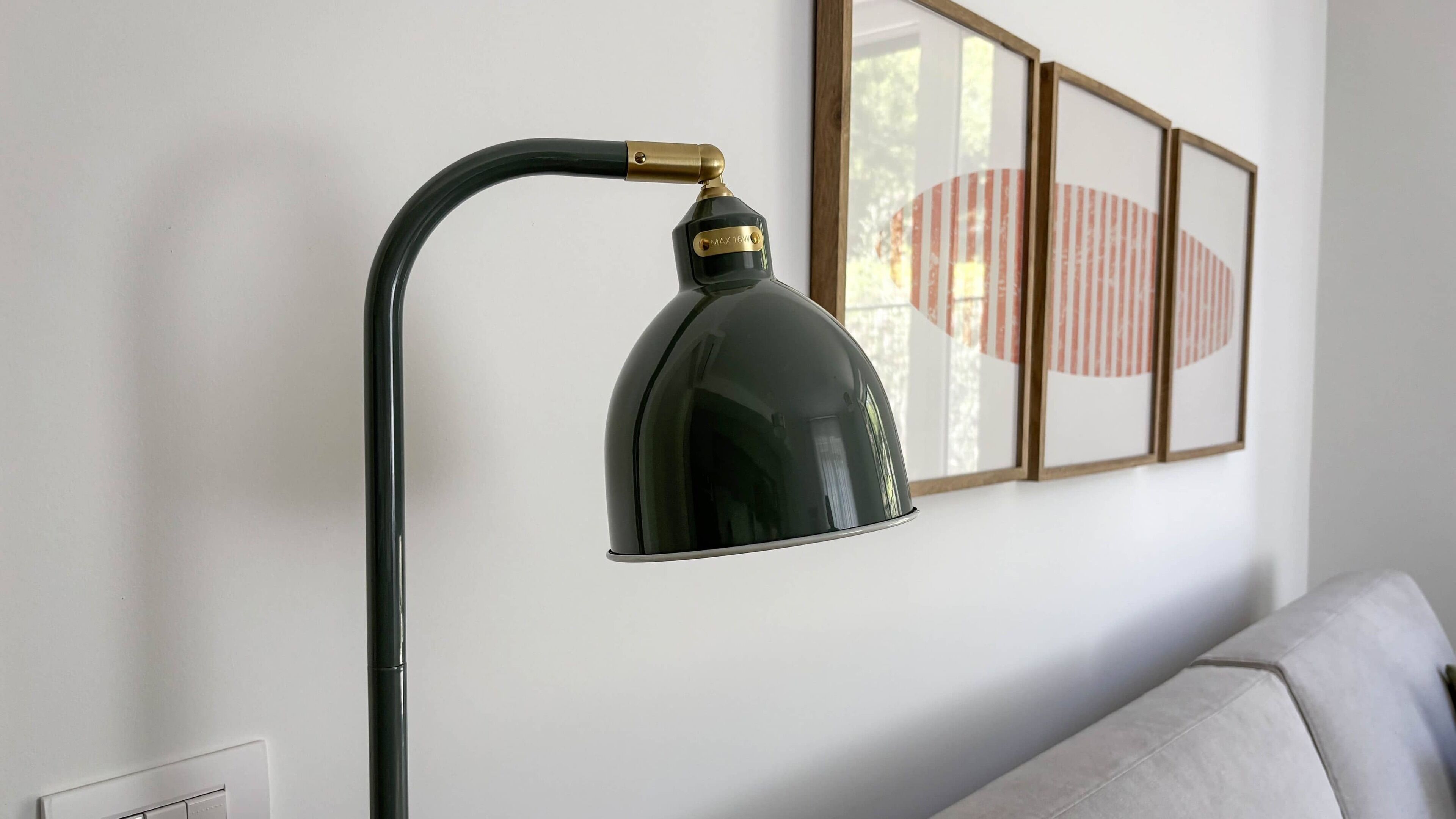 A black desk lamp with a curved arm and a metallic base, mounted on a white wall.