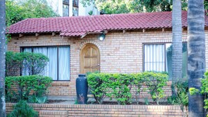A brick house with a red-tiled roof, a wooden door, and a large vase in the front garden. - DREAM NEST (Randburg)