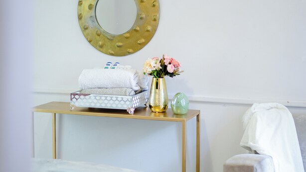 A bathroom with a gold-framed mirror, a small table with towels and toiletries, and a vase with flowers. - DREAM NEST (Randburg)