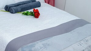 A neatly made bed with a white patterned bedspread, a grey accent strip, and a red rose. - DREAM NEST (Randburg)