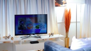 A living room with a flat-screen TV on a white stand, a small table with a basket, and a blue sofa. - DREAM NEST (Randburg)