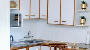 A kitchen with white cabinets, a microwave, a sink, and a wooden chair. - DREAM NEST (Randburg)