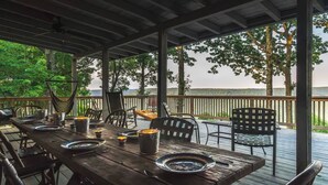 Un espacio cubierto para comer al aire libre con una mesa de madera dispuesta para cuatro personas, rodeada de sillas y con vistas a un paisaje pintoresco.