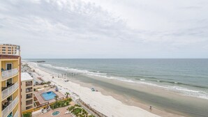 Un hotel frente a la playa con piscina, acceso directo a la arena y un muelle al fondo.