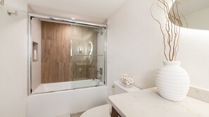 A modern bathroom with a glass-enclosed shower, a white toilet, and a marble countertop with a white vase. - Shores Club 801 - Oceanfront Modern Luxury (Daytona Beach Shores)