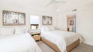 A hotel room with two beds, a window with a view, and artwork depicting palm trees and a beach.