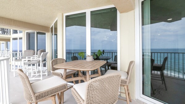 A balcony with wicker furniture, a wooden table, and a view of the ocean.