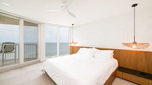 A bedroom with a large bed, a wooden headboard, and a view of the ocean through a sliding glass door.